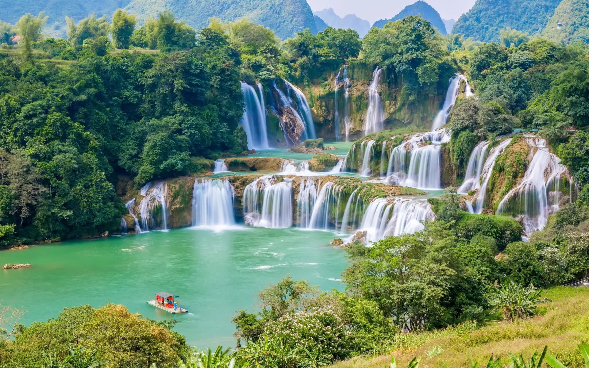 A traditional boat sits in front of the enormous Detail Waterfall in Vietnam.