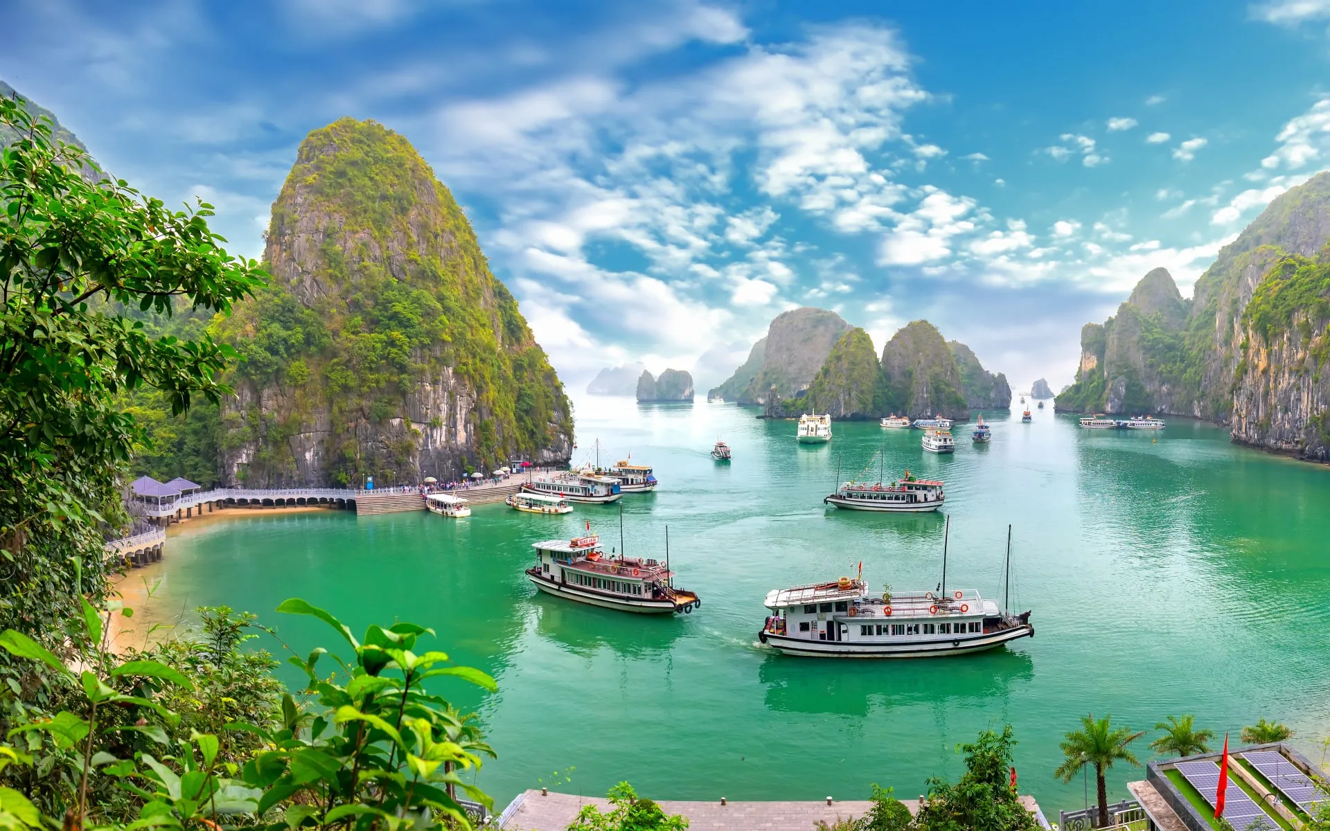 Several large boats sit in the turquoise-green ocean at Ha Long Bay.